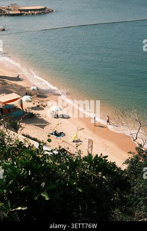 Vista di una spiaggia sabbiosa con ombrelloni colorati, persone che si rilassano sulla sabbia e dolci onde che si infrangono sulla riva di Hong Kong, Hong Kong. Foto Stock