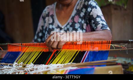 Una vista ravvicinata cattura le mani esperte di un tessitore Mamasa che aziona con cura un tradizionale telaio, tenendo in mano uno strumento di tessitura mentre crea. Foto Stock