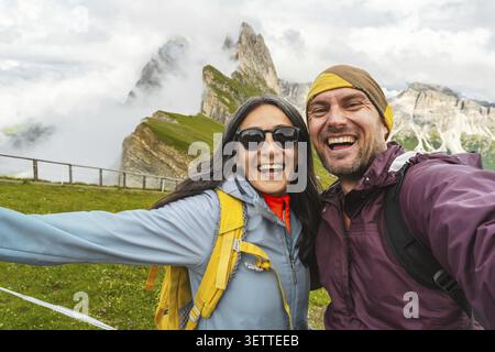 Allegra coppia di amici escursionisti che si fanno selfie nelle montagne delle Dolomiti.Millennial girl che si diverte in una gita estiva di un giorno ridendo insieme alla macchina fotografica Foto Stock