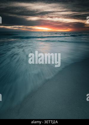 Vista della spiaggia di Mullaloo al tramonto con onde a lunga esposizione che scivolano sulla sabbia a Perth, Australia Occidentale, Australia. Foto Stock