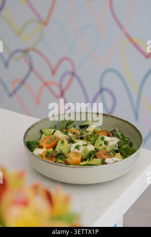 Insalata di verdure miste fresche in una ciotola di ceramica su un tavolo bianco con morbido fondo a cuore pastello Foto Stock