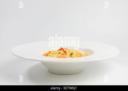Un'appetitosa proposta di pasta mediterranea a base di pesce con succulenti gamberetti, fette di peperoncino rosso piccante ed erbe fresche, elegantemente presentate in un Foto Stock