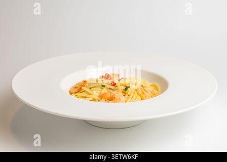 Un'appetitosa proposta di pasta mediterranea a base di pesce con succulenti gamberetti, fette di peperoncino rosso piccante ed erbe fresche, elegantemente presentate in un Foto Stock