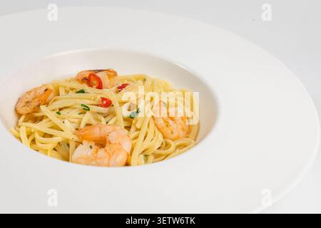 Un'appetitosa proposta di pasta mediterranea a base di pesce con succulenti gamberetti, fette di peperoncino rosso piccante ed erbe fresche, elegantemente presentate in un Foto Stock