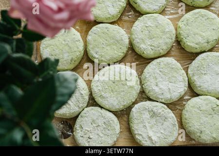 Un primo piano ad alto angolo di frittelle di formaggio cottage cottage crude fatte in casa mescolate con erbe verdi, preparate per la frittura e decorate con bellissime freschissime Foto Stock