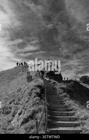 Gli escursionisti saliranno una scala all'aperto in pietra verso la cima della cresta di Stoos in bianco e nero Foto Stock