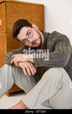Il giovane con la barba mostra un look casual mentre è seduto in un ambiente da studio Foto Stock