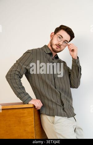Questo giovane uomo sfoggia il suo elegante outfit casual in un moderno ambiente da studio Foto Stock