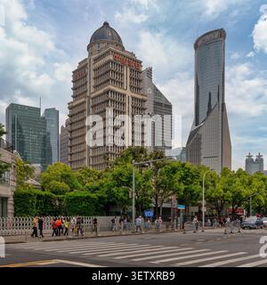 Shanghai, Cina - 4 maggio 2026: Moderni grattacieli, tra cui il Ping An Financial Center e la torre della Bank of China, si innalzano sopra una trafficata strada urbana con pedoni e alberi verdi nel quartiere di Lujiazui Foto Stock