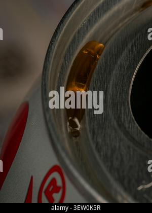 Primo piano di un liquido ambrato riunito nella scanalatura superiore e sul bordo metallico di una barattola in alluminio, foto astratta del brodo Foto Stock
