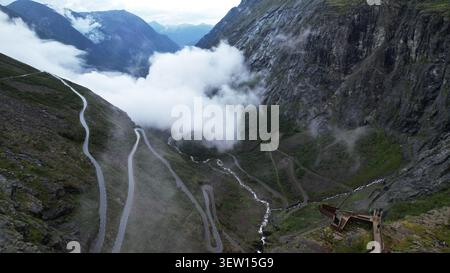 Spettacolare vista in droni della famosa strada di montagna Trollstigen che si snoda attraverso un ripido terreno alpino, con nuvole basse, valli profonde, cascate e sceni Foto Stock