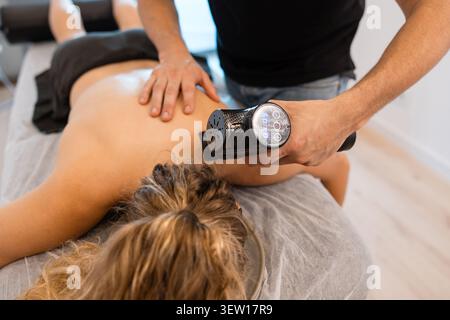 Terapista che tratta il paziente con una pistola per massaggi a percussione Foto Stock