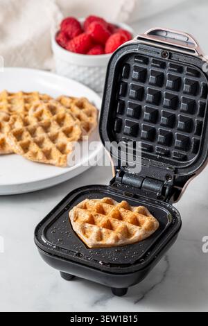 Un mini waffle appena fatto a forma di cuore su una mini macchina per waffle. Foto Stock