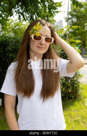 Giovane donna che indossa eleganti occhiali da sole con fiori selvatici in Hair Outdoors Foto Stock