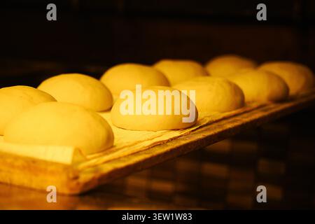 L'impasto del pane si solleva su un vassoio di legno in una cucina calda Foto Stock