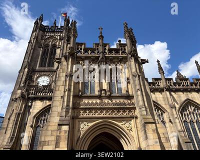 Vista esterna dall'angolo basso della Cattedrale di Manchester nel centro città, Manchester, che mostra muratura in pietra tardo gotica, torre dell'orologio e gargoyle. Foto Stock