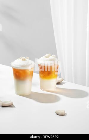 Bevande rinfrescanti a strati di caffè freddo in bicchieri di plastica trasparenti su sfondo bianco minimalista con ombre Foto Stock