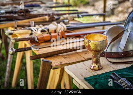 Una varietà di spade antiche, asce e mazze sono esposte su una superficie rustica in legno, evocando un senso di combattimento e artigianato storico Foto Stock
