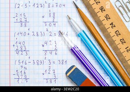 Righello, matita, penne, gomma e graffette sullo sfondo di un quaderno scolastico in matematica. Cartoleria sullo sfondo della risoluzione di mathematica Foto Stock