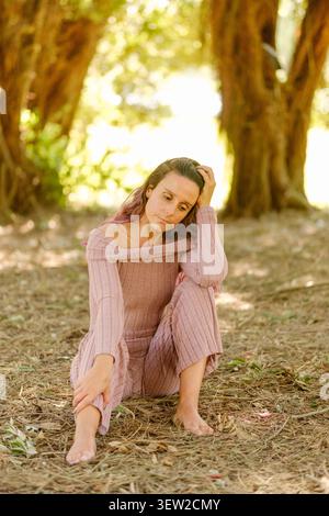 Donna pensiva seduta su un terreno boschivo asciutto in un ambiente rurale all'aperto Foto Stock