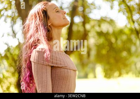 Donna con gli occhi chiusi che trova pace e relax all'aperto alla luce del sole Foto Stock
