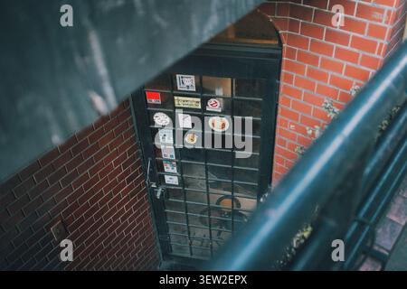 Vista ad alto angolo di una porta d'ingresso in vetro d'epoca adornata con adesivi pop in un edificio in mattoni a Shimokitazawa Foto Stock