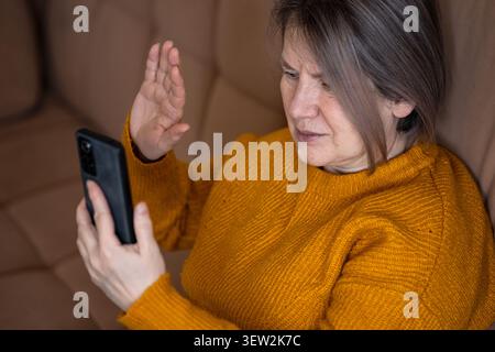 Donna matura che ha una videochiamata sullo smartphone, che saluta la mano Foto Stock
