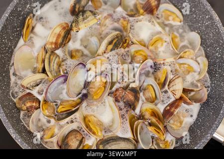 Cuocere le vongole in una padella a casa. Primo piano di vongole sospese nel vino bianco. Foto Stock