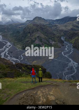 Vista aerea della valle di Thorsmork con due escursionisti che si trovano su una scogliera che si affaccia su fiumi intrecciati, sabbia vulcanica scura e aspre montagne di Hvols Foto Stock