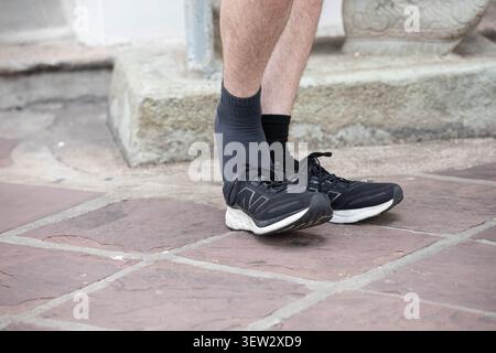 BANGKOK, THAILANDIA - 3 giugno 2026: L'uomo sta per indossare sneakers nere, vista dall'alto. Foto Stock