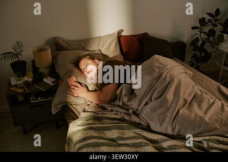 Una donna di dimensioni più grandi che dorme tenendo in mano lo smartphone a letto di notte Foto Stock