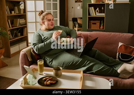 Plus size Woman pranza mentre usa il laptop su un divano a casa Foto Stock