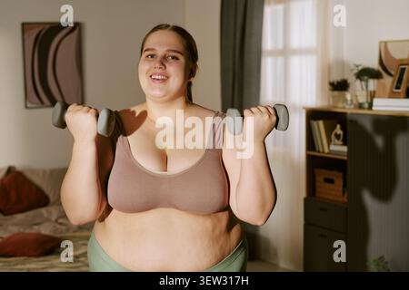 Ritratto della donna Plus size che si esercita con i manubri a casa Foto Stock