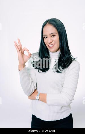 Donna asiatica sorridente mostrando OK mano gesto su sfondo bianco Foto Stock
