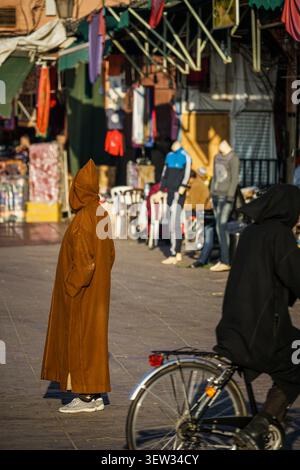 Marrakech, Marocco - 3 dicembre 2017: Una persona che indossa una tradizionale djellaba con cappuccio marrone si erge di fronte alla macchina fotografica in un vivace marocchino Foto Stock