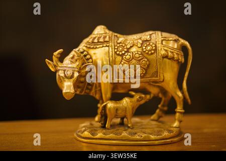 Figurina in ottone di mucca e vitello dorata su superficie di legno con sfondo scuro Foto Stock