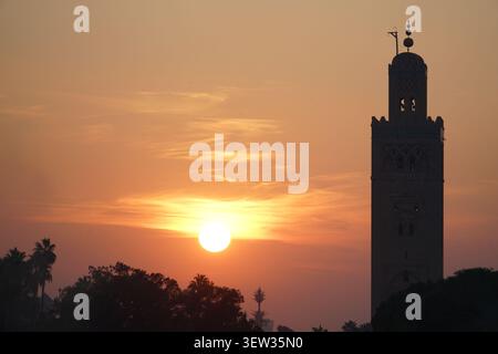 Il minareto della Moschea di Koutoubia è modellato contro il tramonto del sole e il cielo arancione a Marrakech, in Marocco, con palme visibili sotto. Questa immagine è S Foto Stock
