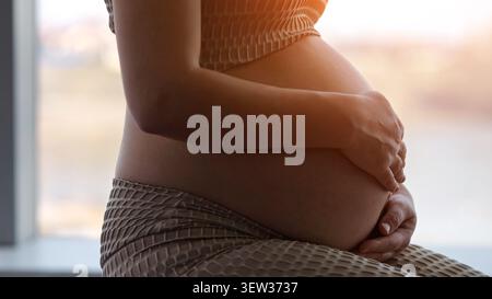 Donna incinta che tiene dolcemente la pancia sentendo maternità Foto Stock