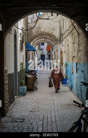 MAROCCO, ESSAOUIRA - 5 dicembre 2017: Una donna in tradizionale abito marocchino cammina lungo uno stretto vicolo arcuato nella medina di Essaouira. I ciottoli Foto Stock