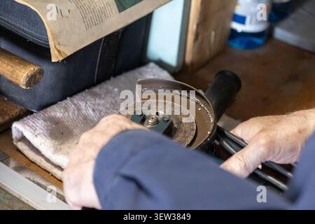 Il tecnico esegue il fissaggio di una mola su un utensile elettrico in un'officina, evidenziando un'attenta manutenzione e l'esperienza meccanica in un esperto p Foto Stock
