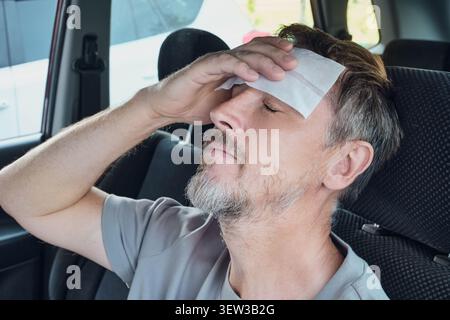 Un uomo che si sente male e ha la febbre, riposa la testa con una placca rinfrescante Foto Stock