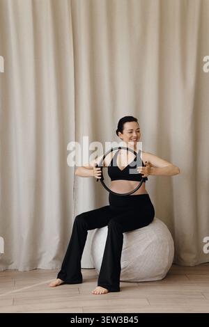 Donna incinta che tiene in mano pilates seduti sulla palla fitness durante l'allenamento Foto Stock