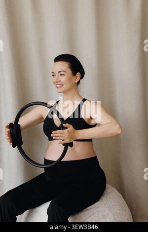 Donna incinta che tiene in mano pilates seduti sulla palla fitness durante l'allenamento Foto Stock