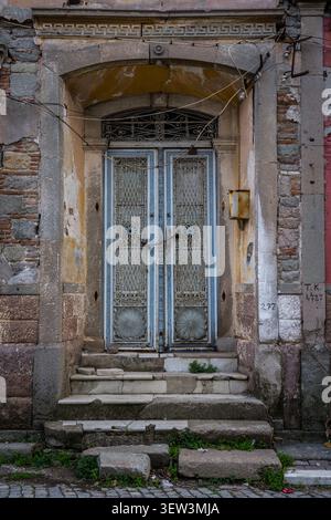 Una vista ravvicinata di una doppia porta blu antica fatiscente con griglie in metallo ornate e motivi circolari, collocata all'interno di un arco in pietra intemprata. Usura Foto Stock