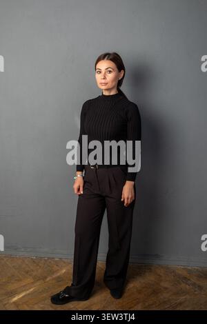Donna di successo in piedi vicino al muro grigio. Ritratto di architetto o interior designer di mezza età. Donna d'affari professionale vestita di tartaruga nera Foto Stock
