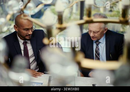 Uomini d'affari di mezza età che esaminano i documenti durante la riunione dell'industria petrolifera, discutono della strategia e della pianificazione della partnership. Ideale per la leadership nel settore energetico, gli investimenti e il marketing di consulenza Foto Stock