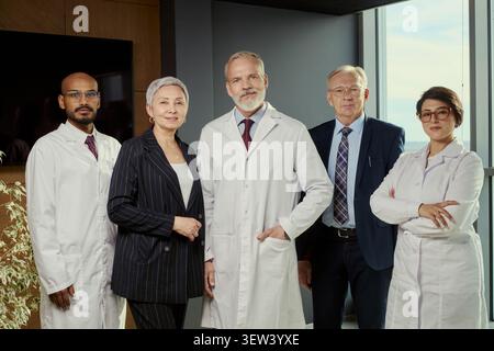 Ritratto di diverse squadre mediche di mezza età e di anziano in piedi insieme in clinica, presentando leadership e competenza. Ideale per personale sanitario, branding ospedaliero, campagne di fiducia Foto Stock