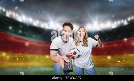 Famiglia di tifosi di calcio che accendono una partita di calcio utilizzando il telecomando sul televisore. campo da calcio testurizzato con nebbia neon - centro, centrocampo. Foto Stock