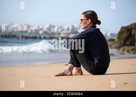 Donna contemplativa seduta su Sandy Beach affacciata sul mare Foto Stock
