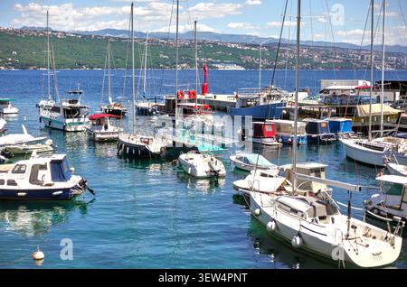 Porto locale pieno di yacht ormeggiati, barche a vela e motoscafi in una giornata di sole a Abbazia, Croazia, con colline costiere sullo sfondo. Foto Stock